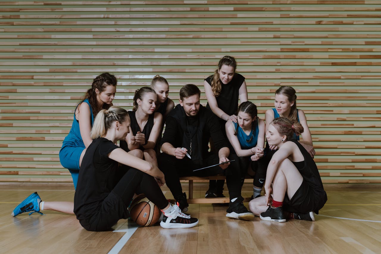 A coach strategizes with a womens basketball team in a gymnasium.